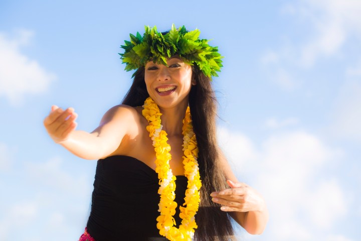 A beautiful Hawaiian Hula dancer dancing on the beach of the tropical Hawaiian islands. She is wearing a contemporary Hula dance dress with a lei and flower headdress. Photographed in horizontal format with copy space in Kauai, Hawaii.