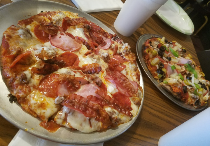 Two pizzas, one with strips of bacon, ham and pepperoni, and the other all veggies.
