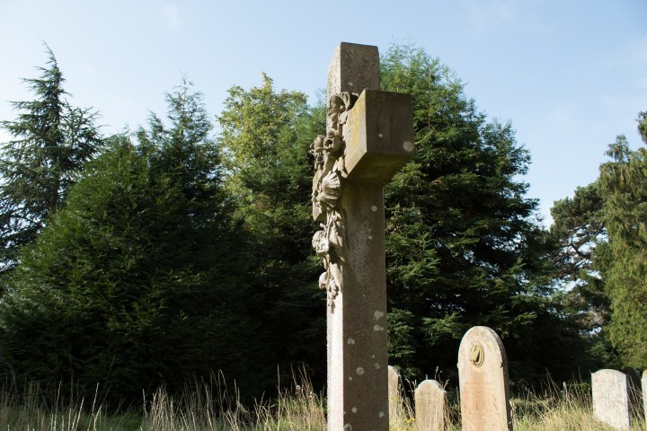 Cross grave marker in a spooky cemetery with headstones in the background