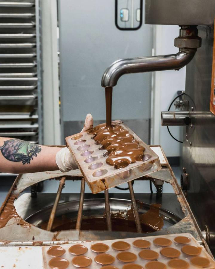 Chocolate pours out of a chocolate fountain to cover fresh made chocolate bonbons at French Broad Chocolates in North Carolina