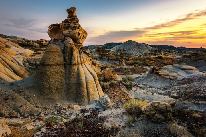 A colorful sunset in Makoshika State Park illuminates a tall rock formation.