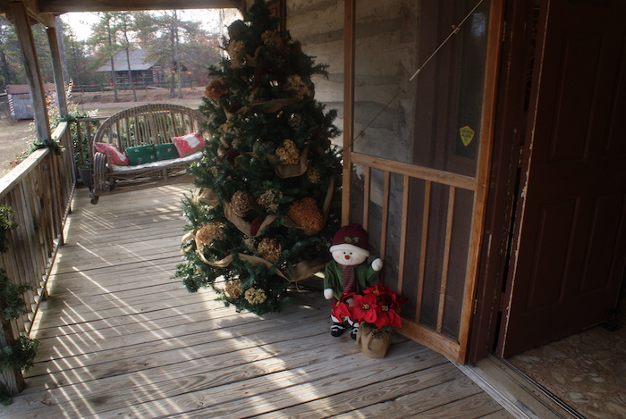 A decorated Christmas tree on a cabin porch and open door welcoming guests inside at LaGrange Historic Site