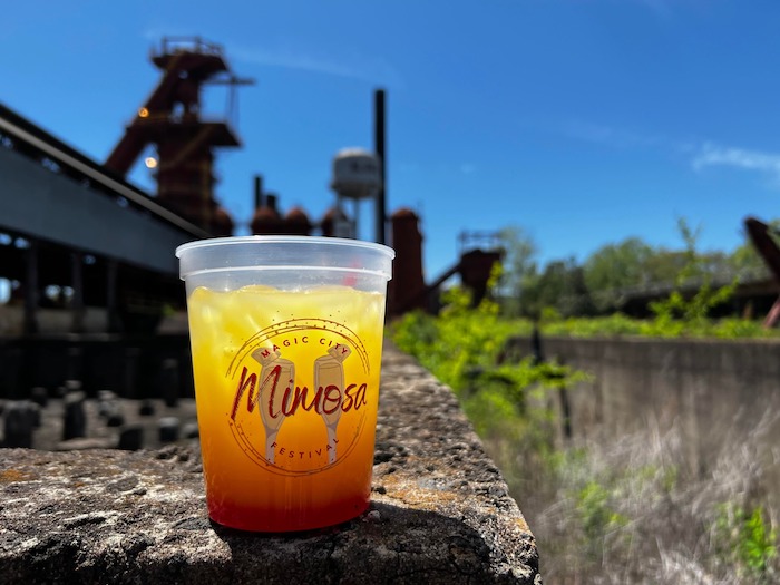 A mimosa in a cup with Sloss Furnaces in the background in a promotional image for the mimosa festival in Birmingham, Alabama
